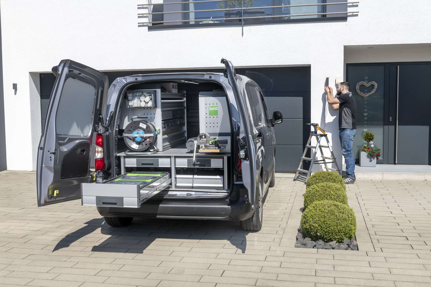 Une camionnette avec des portes arrière ouvertes montre différents aménagements de véhicules, y compris des étagères et des extensions de charge pour des tiroirs professionnels dans des véhicules utilitaires.