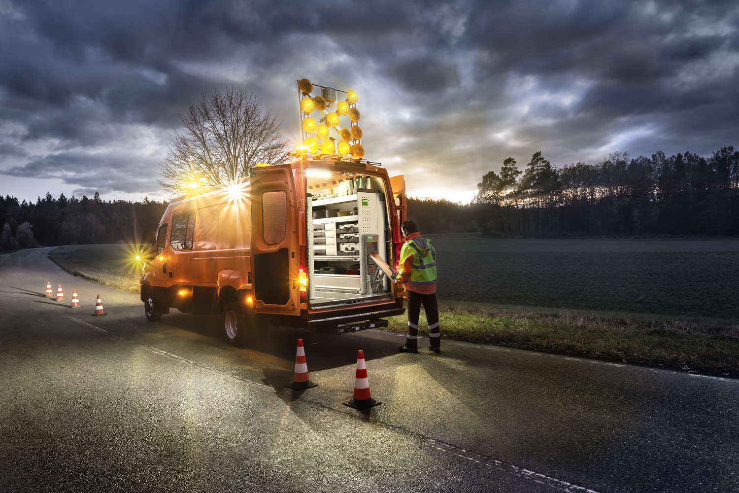 Une camionnette est garée au bord de la route avec des feux de détresse et sécurise une zone dangereuse.